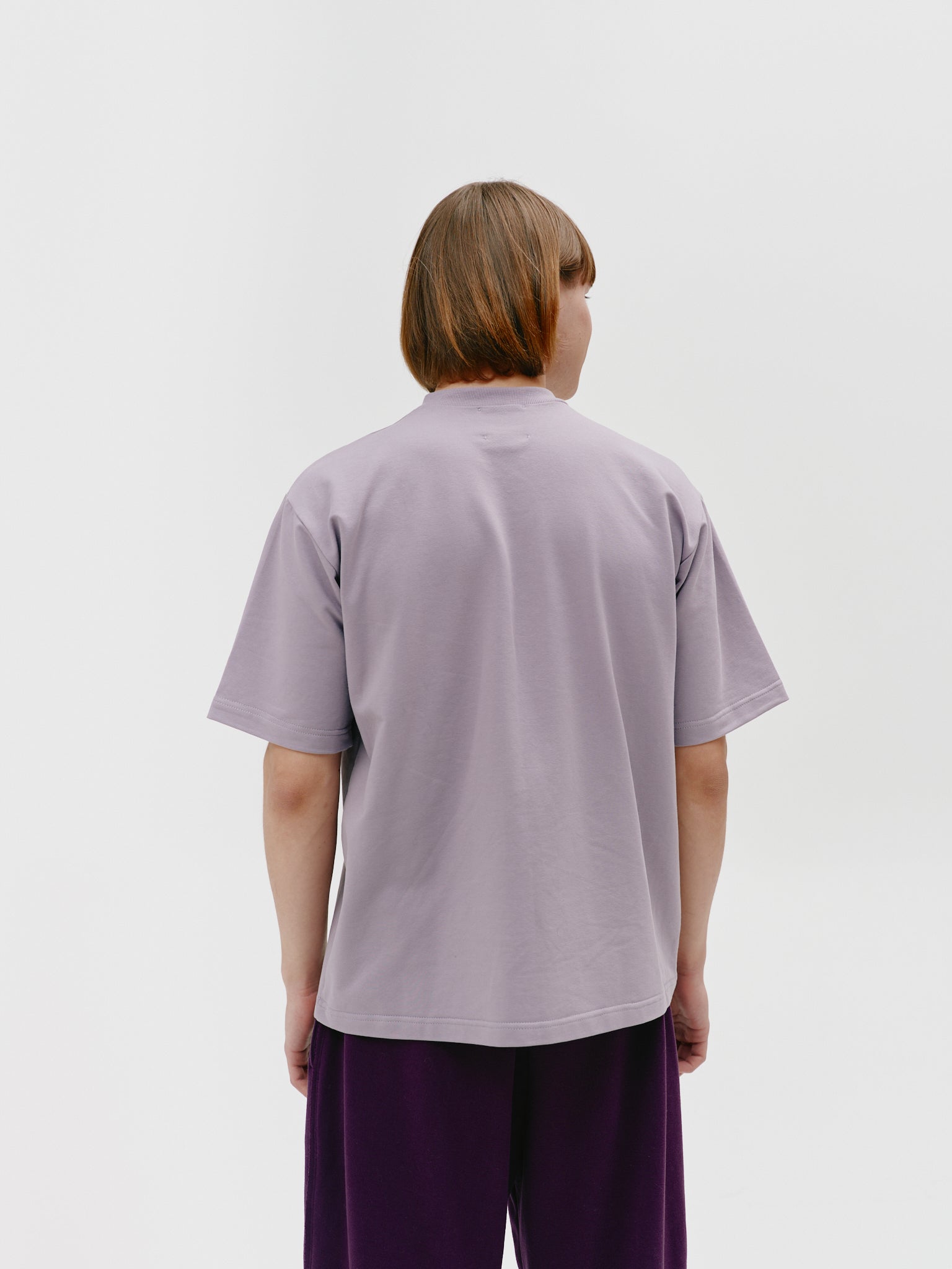 Model standing with back to camera, wearing a dark grey unisex cotton t-shirt with a stand-up collar, showcasing its comfortable and stylish fit