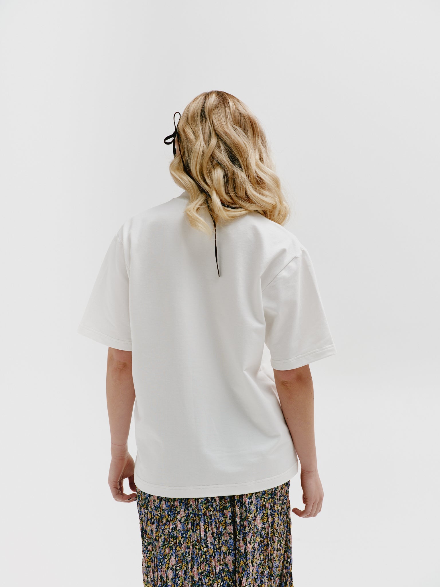 Model standing with back to camera, wearing a white unisex cotton t-shirt with a stand-up collar and refined embroidery