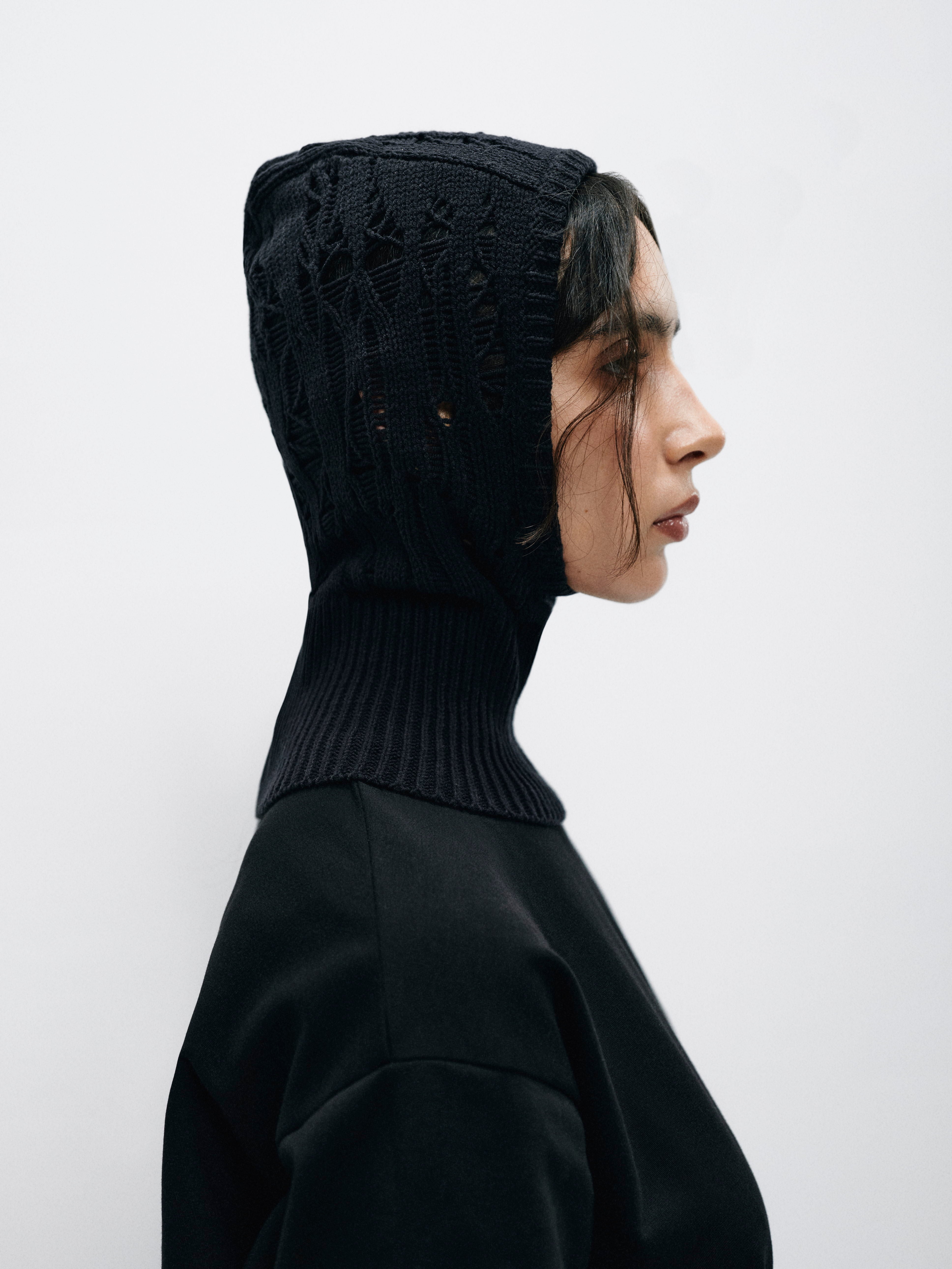 Front view of a cotton balaclava with intricately intertwined knitted panels, showcasing its unique textured design