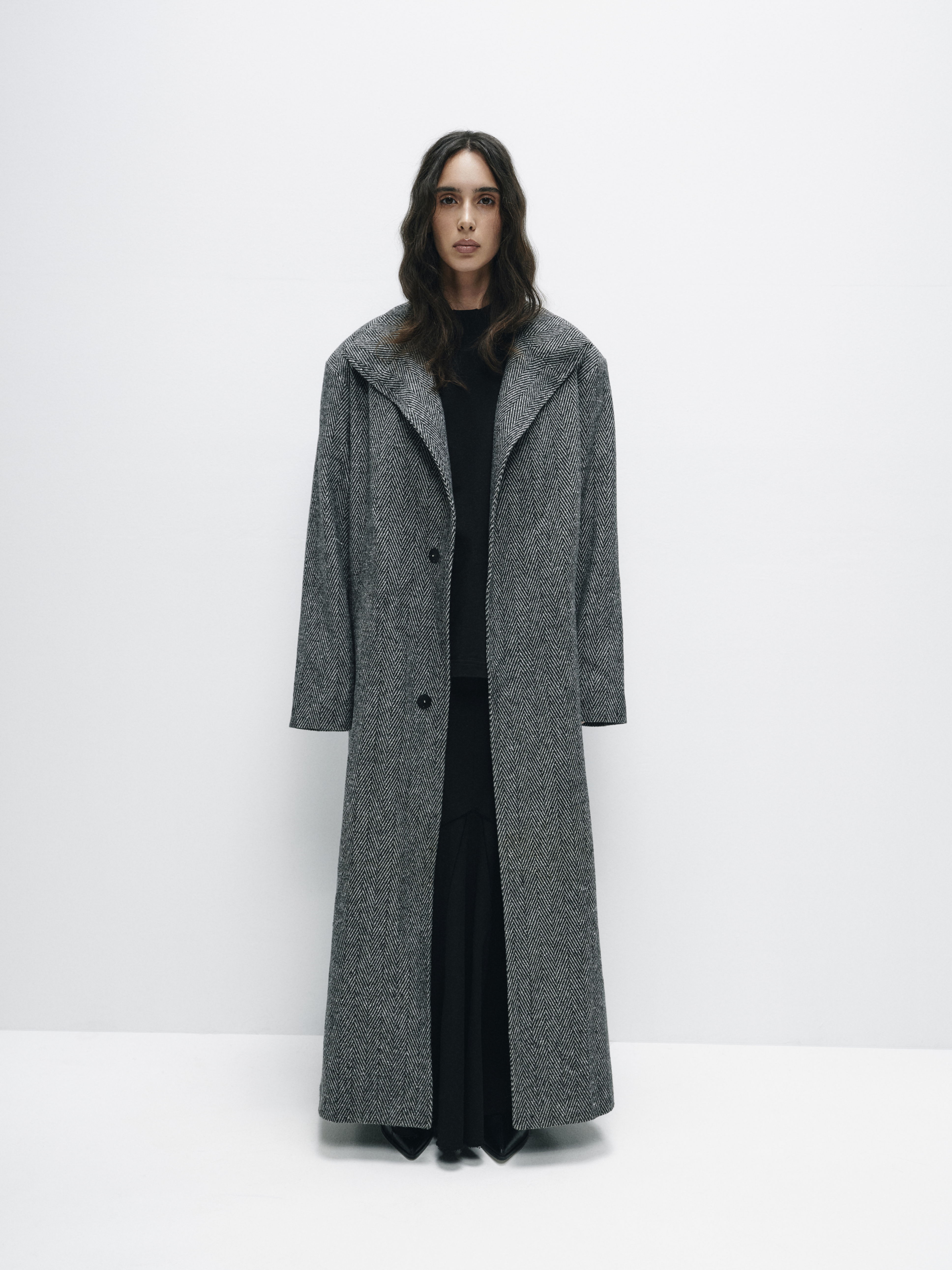 Front view of the floor-length coat with broad shoulders, highlighting its elegant silhouette and structured design