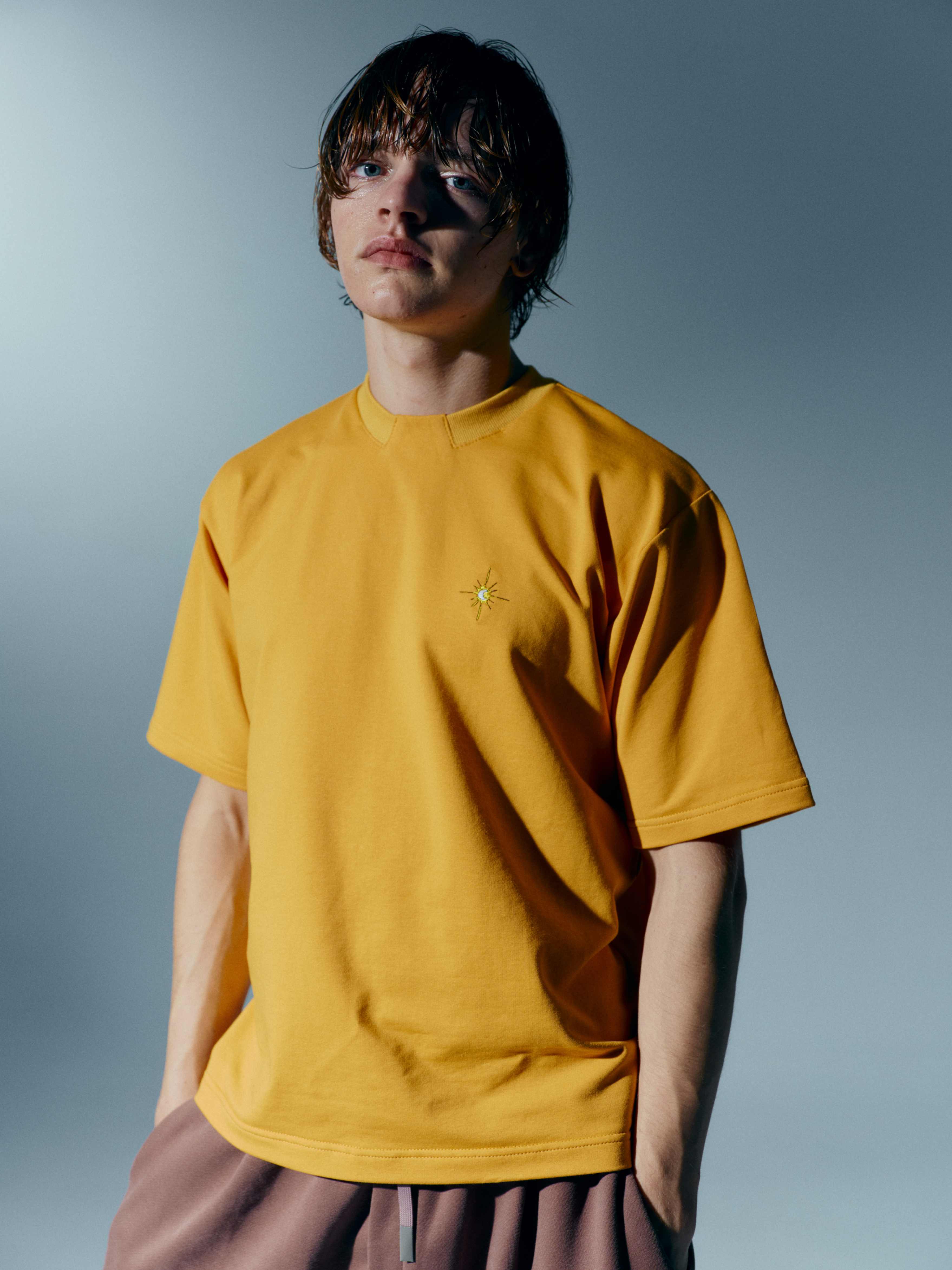 Model standing front view in a mustard yellow unisex cotton t-shirt with a stand-up collar and detailed embroidery, blending casual style with sophistication