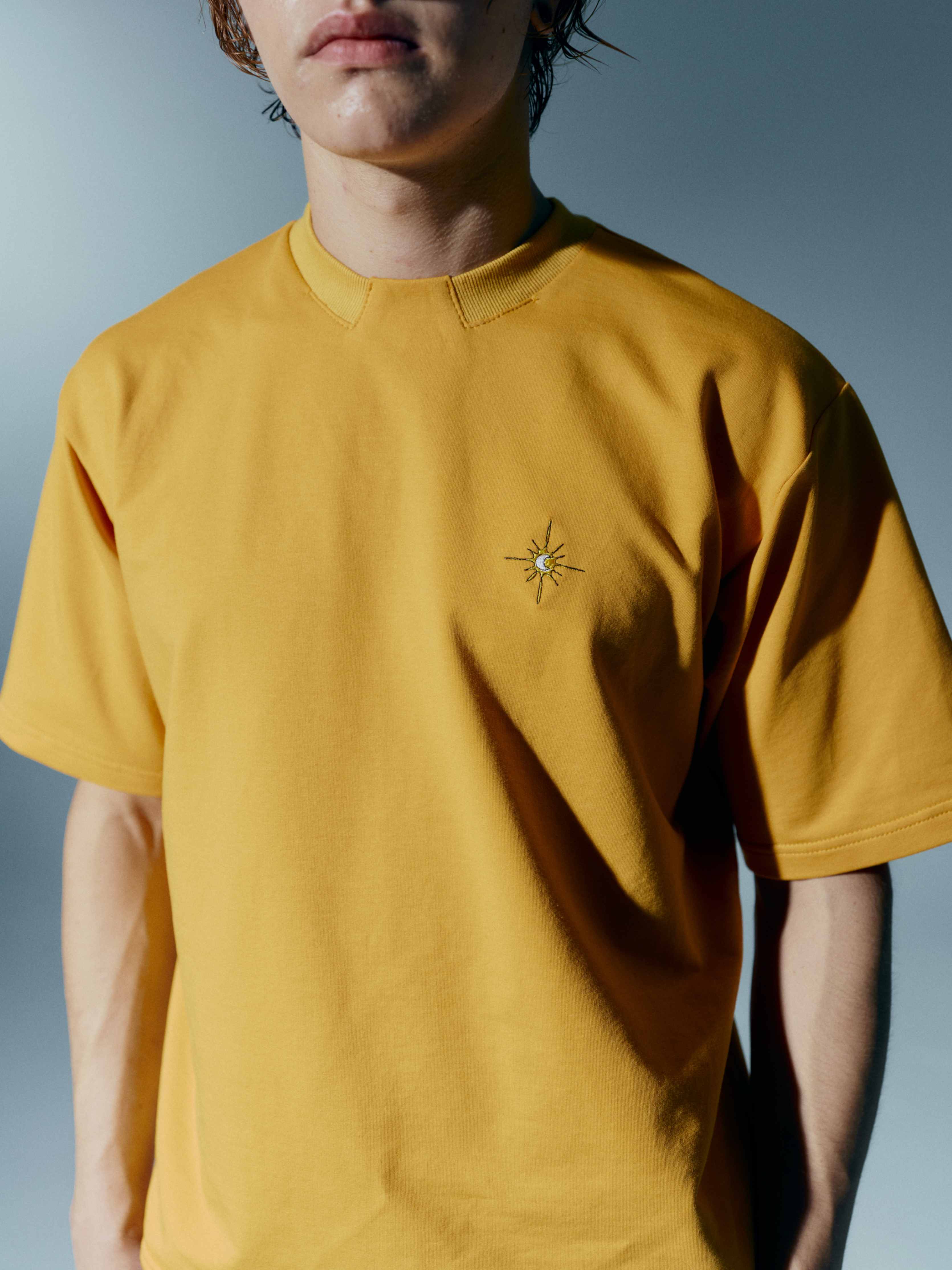 Close-up of a mustard yellow unisex cotton t-shirt, highlighting the stand-up collar and embroidery details, offering a stylish twist to a classic tee